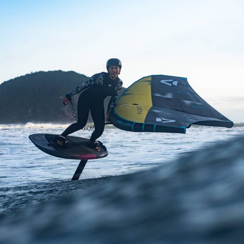 Rider en action avec l’aile Duotone Float 2025 en wingfoil dans les vagues, portant une combinaison et un casque, en pleine session de downwind