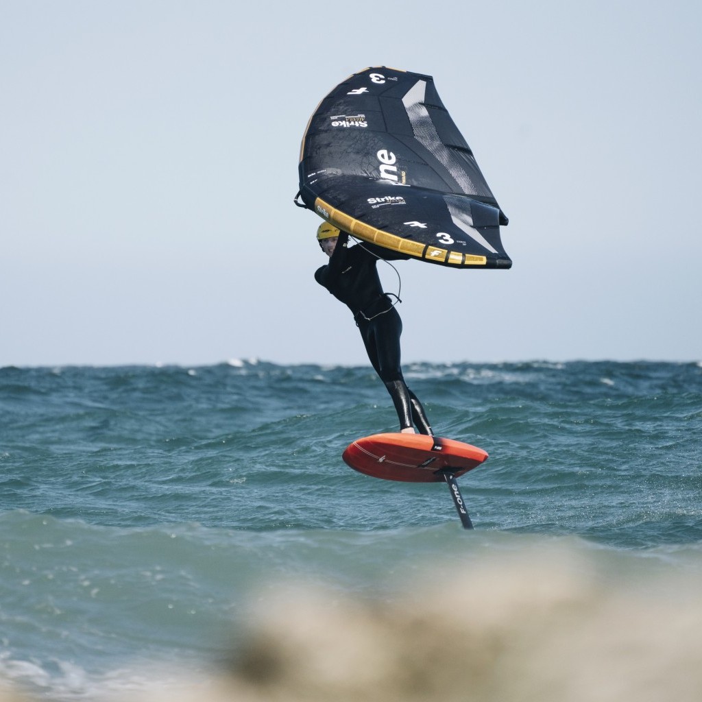 Rider pratiquant le wingfoil sur une mer agitée avec une aile F-One Strike V5.
