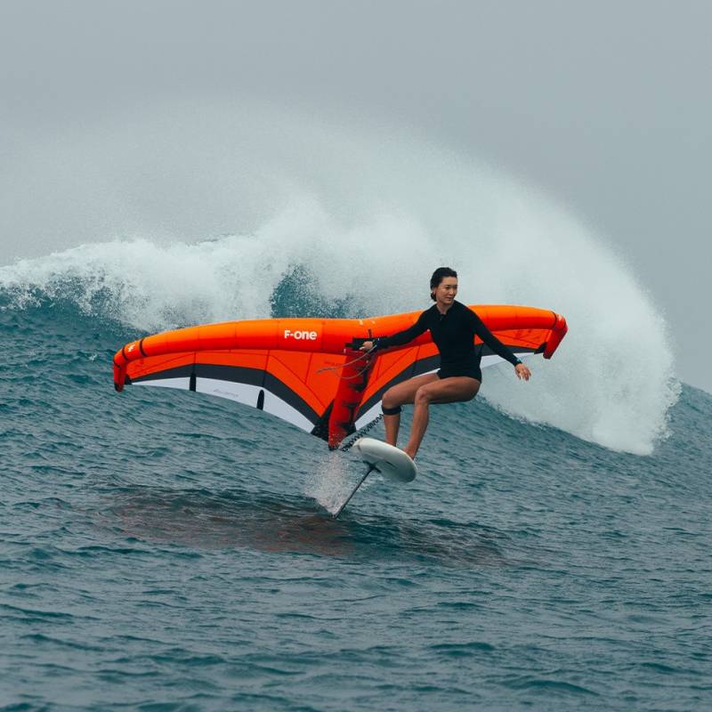 Rider en foil utilisant la F-ONE Strike V5 orange dans les vagues – aile puissante idéale pour surf, vitesse et cap performant